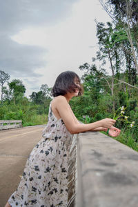 Side view of young woman standing by road against sky