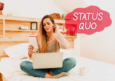 Young woman using phone while sitting on laptop