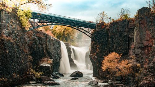 View of waterfall along plants and bridge