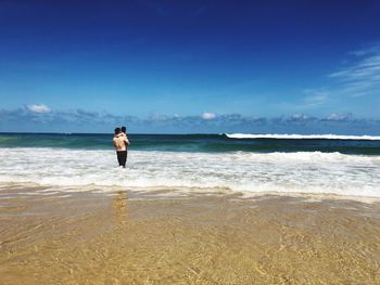 Father carrying daughter in sea against blue sky