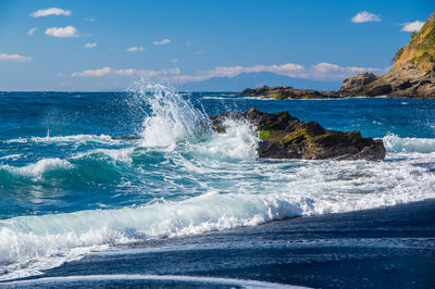 Scenic view of sea against sky with waves crashing against rock.