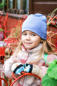 A young girl with blonde hair smiles in a blue hat with white polka dots.