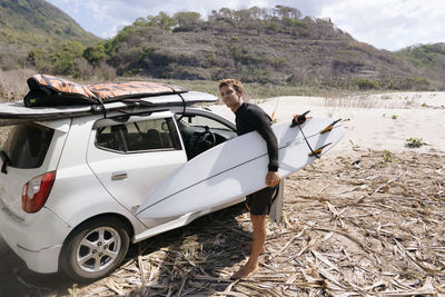 Young man with surfboard near car