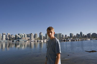 Teenage boy standing against buildings in city during sunny day
