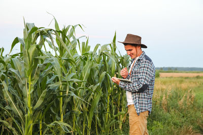 Agro tech tablet. caucasian calm male maize grower in overalls walks along corn field with tablet pc