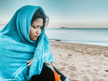 Woman wrapped in towel while sitting at beach