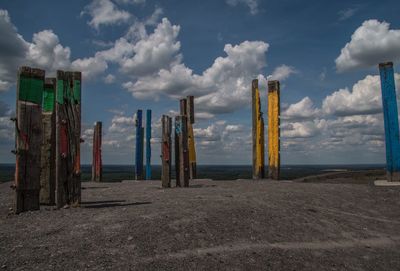 Wooden posts on field against cloudy sky