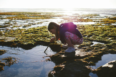 Rear view of girl on rock at beach against sky