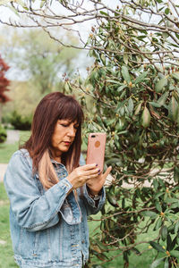 Woman using smart phone while standing by plants