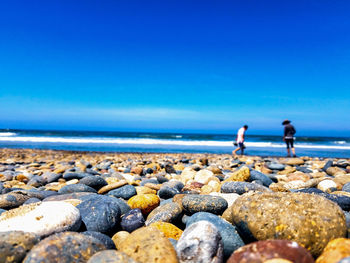 People on rocks at beach against blue sky