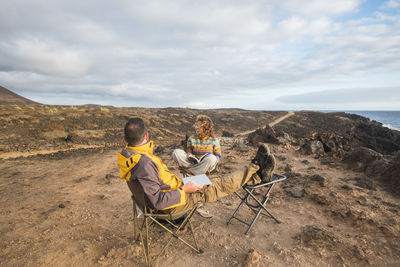 Friends sitting at beach against sky