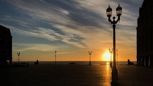 Silhouette street light by sea against sky during sunset