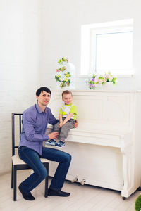 Father and son sitting on man against wall