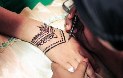 Cropped hand of woman getting henna tattoo