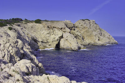 Rock formations in sea against clear blue sky