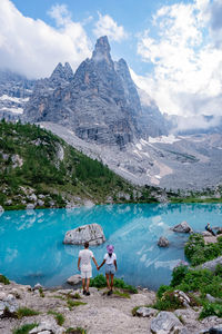 People on lake by mountains against sky