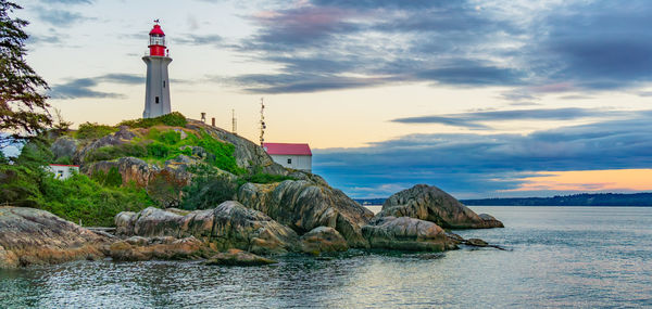 Lighthouse by sea against sky during sunset