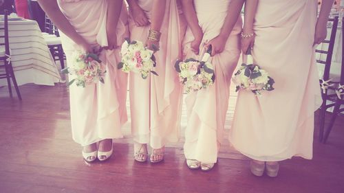 Low section of bridesmaids with bouquets standing on hardwood floor