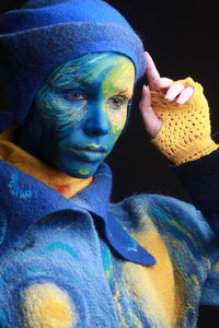 Close-up of young woman with painted face against black background