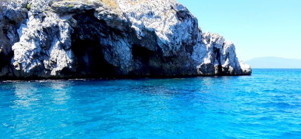 Rock formation in sea against clear blue sky