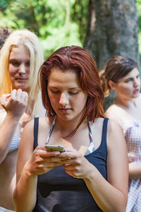 Young woman using mobile phone against friends