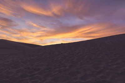Sand dunes in desert by cloudy sky