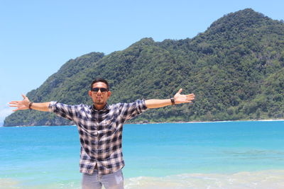 Man with arms outstretched standing by sea against mountains