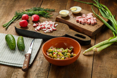 Okroshka in a clay plate on a table on a wooden table next to vegetables on boards and a knife