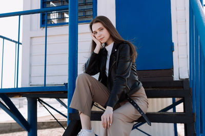 Young woman using phone while sitting on railing