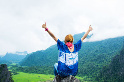 Rear view of female hiker gesturing thumbs up while sitting on rock