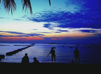 Silhouette people on beach against sky during sunset