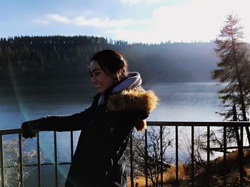 Smiling young woman standing at observation point by lake during winter