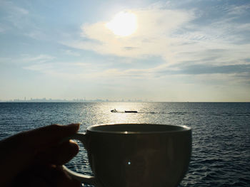 Person holding drink by sea against sky