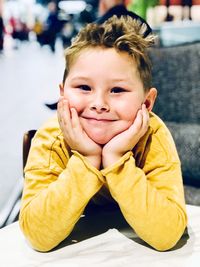 Portrait of smiling boy with hand on chin sitting at sidewalk cafe in city