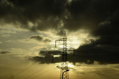 Low angle view of electricity pylon against sky during sunset