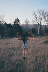 Rear view of woman jumping on field against sky