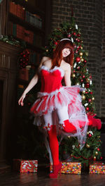 Portrait of woman standing on one leg against christmas tree