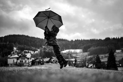 Boy with umbrella jumping on road against sky