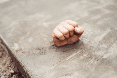 High angle view of clenched fist coming out from concrete