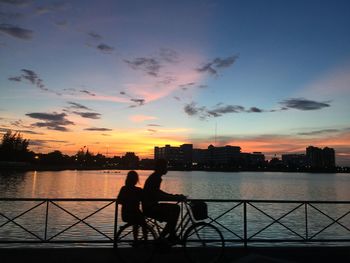 Silhouette people on riverbank against sky during sunset