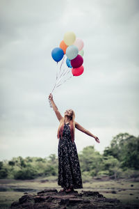 Full length of woman holding balloons while standing against sky