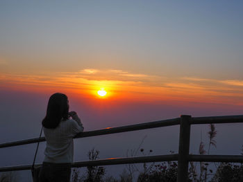 Rear view of woman photographing against sky during sunset