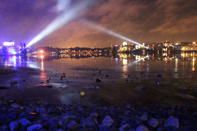 Illuminated city by sea against sky at night