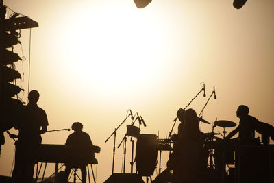 Silhouette artists at music concert against sky during sunset