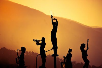 Silhouette statues against mountain during sunset