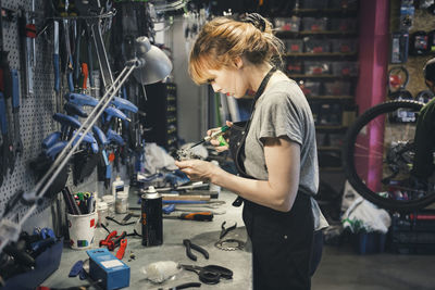 Side view of female mechanic oiling pedal in workshop