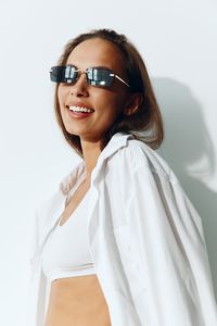 Portrait of young woman wearing sunglasses while standing against white background