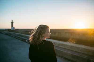 Woman looking away at promenade against clear sky during sunset