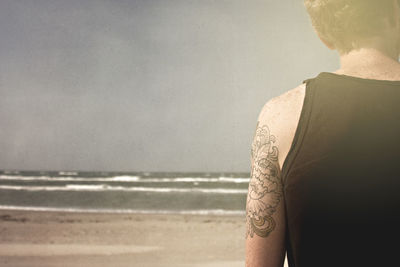 Cropped image of man standing on shore at beach against clear sky