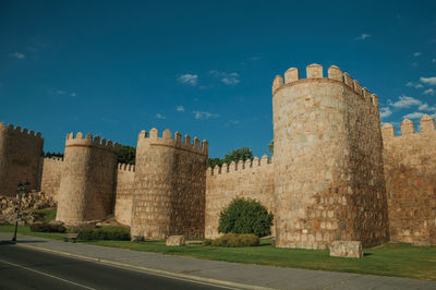 Street and light posts beside stone towers in the large wall encircling the town of avila, in spain.